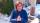 Une femme rousse portant une veste bleue, assise dans un jardin enneigé.